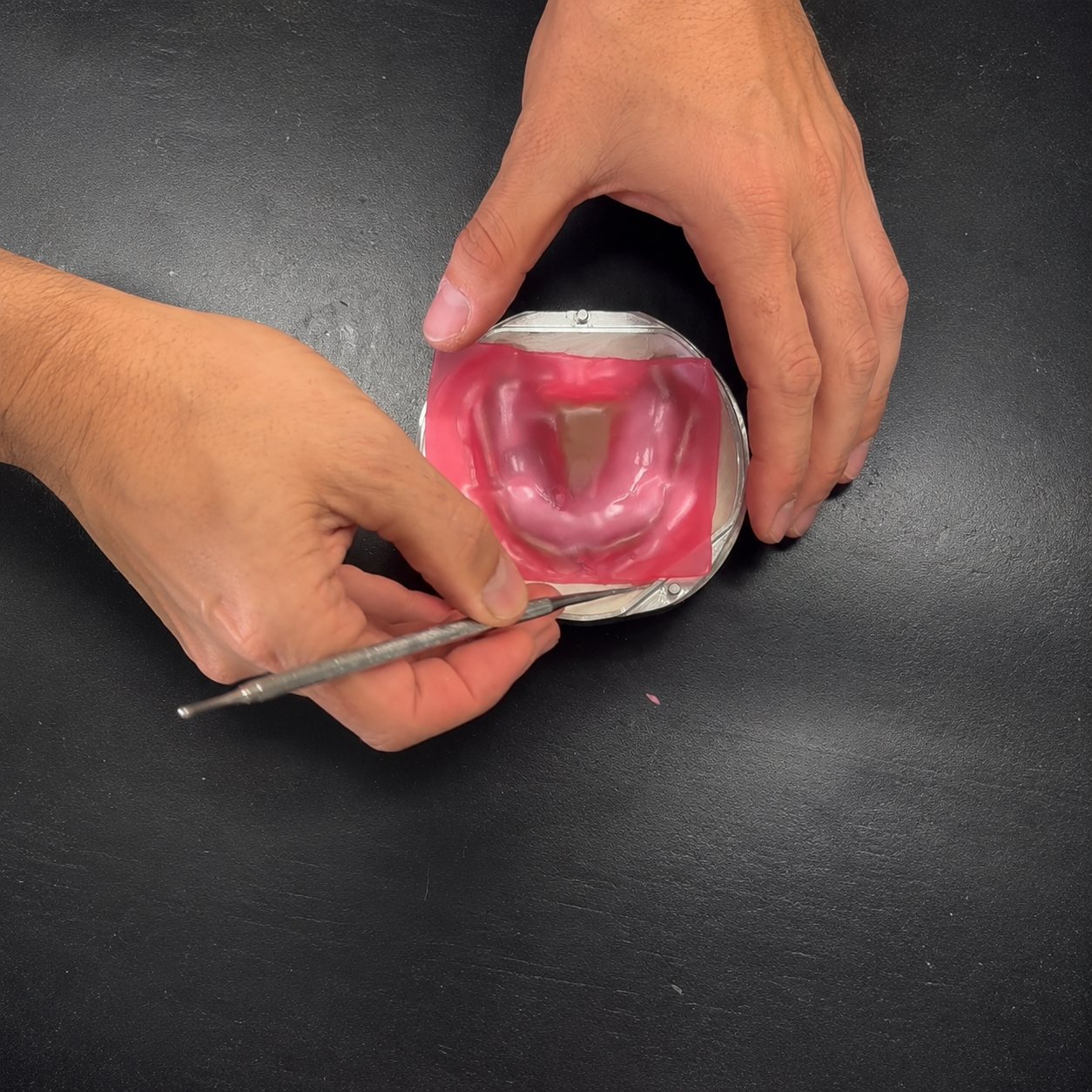 Hands adapting a pink wax spacer onto the prosthetic in the flask